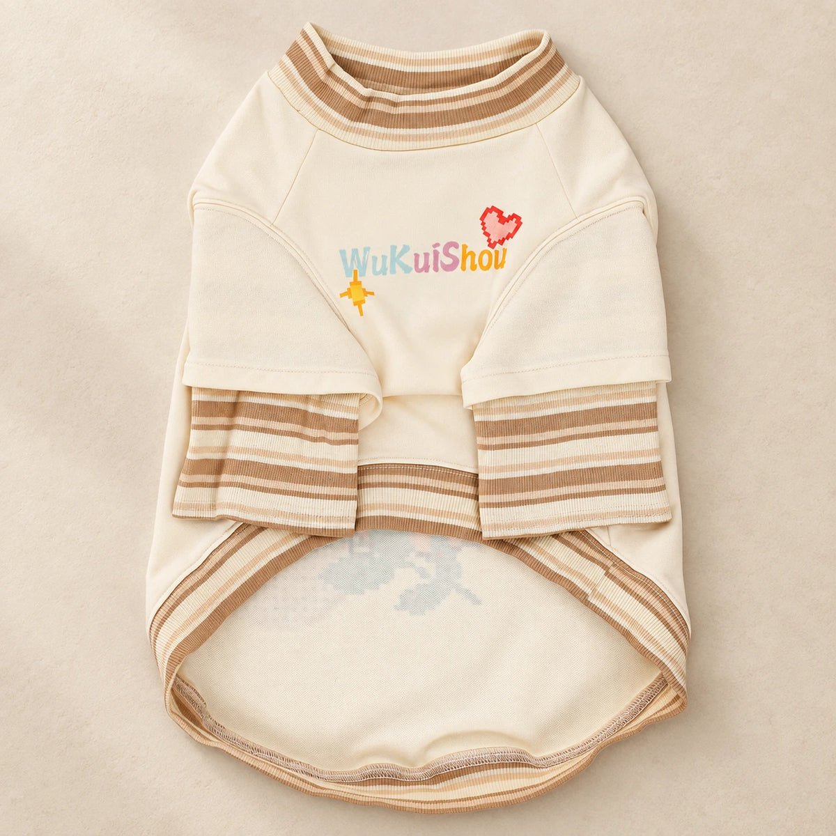 Front and underside product view of the cream pet top, with joined striped sleeves, a ribbed neckline and WUKUISHOU chest lettering. AI-edited background.